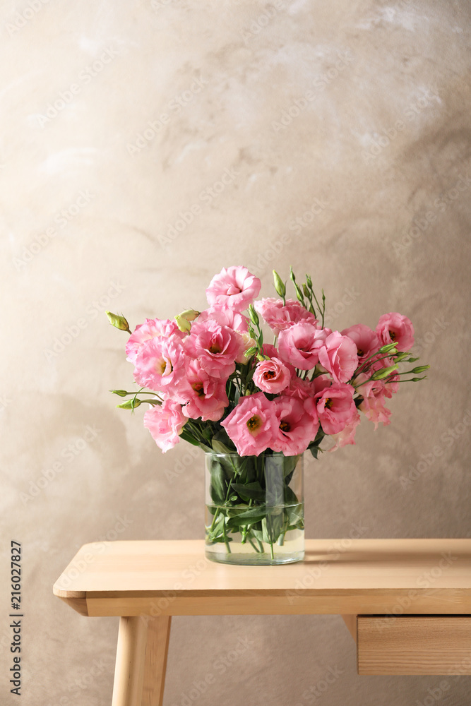 Vase with beautiful Eustoma flowers on table against color background