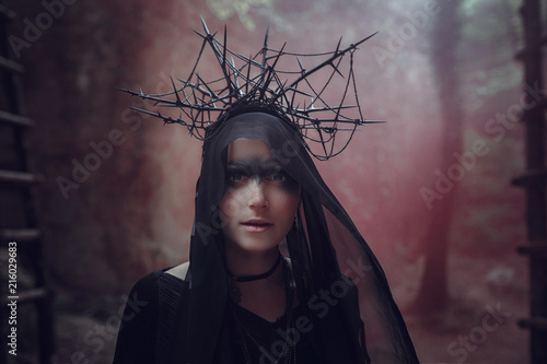 A beautiful woman with pale skin in a black dress and in the black crownk. Gothic look. Outfit for halloween.