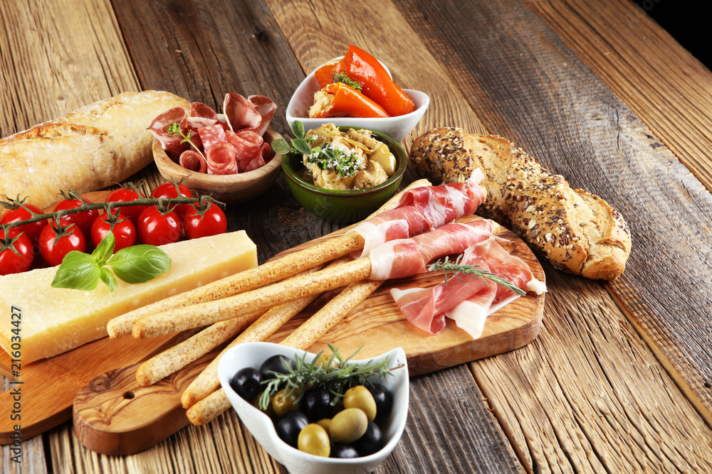 Italian antipasti wine snacks set. Cheese variety, Mediterranean olives, crudo, Prosciutto di Parma, salami and wine in glasses over wooden grunge background. Italian antipasti wine snacks set. Cheese variety, Mediterranean olives, crudo, Prosciutto di Parma, salami and wine in glasses over wooden grunge background.