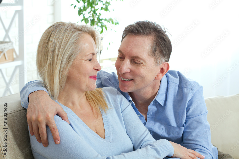 Middle aged couple relaxing on the couch smiling at camera at home in the living room Middle aged couple relaxing on the couch smiling at camera at home in the living room