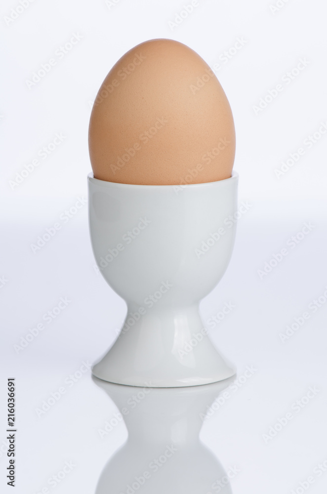 Brown egg in white porcelain cup, partial silhouette in foreground. Brown egg in white porcelain cup, partial silhouette in foreground.