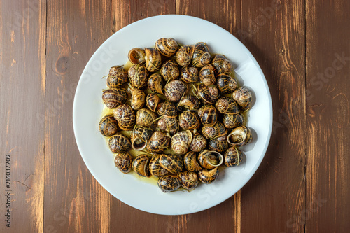 Tasty fried snails in white dish on brown wooden background.