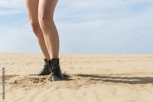 Slender female legs in boots, standing in the sand in the desert, close-up