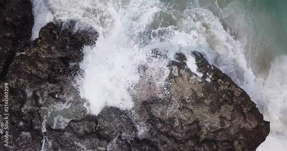 Aerial top view waves break on dark rocks near beach. Sea waves on the dangerous stones aerial view drone 4k shot. Bird's eye view of ocean waves crashing against an empty beach from above. Aerial top view waves break on dark rocks near beach. Sea waves on the dangerous stones aerial view drone 4k shot. Bird's eye view of ocean waves crashing against an empty beach from above.