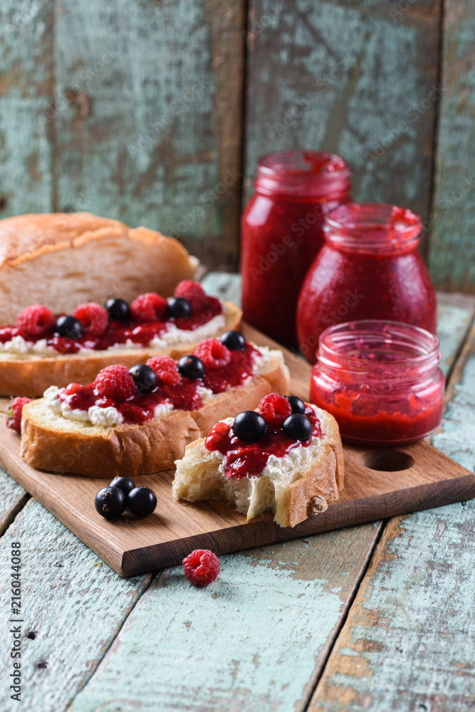 Tasty summer breakfast. Ciabatta toasts with homemade raspberry jam served with raw berries on shabby blue background
