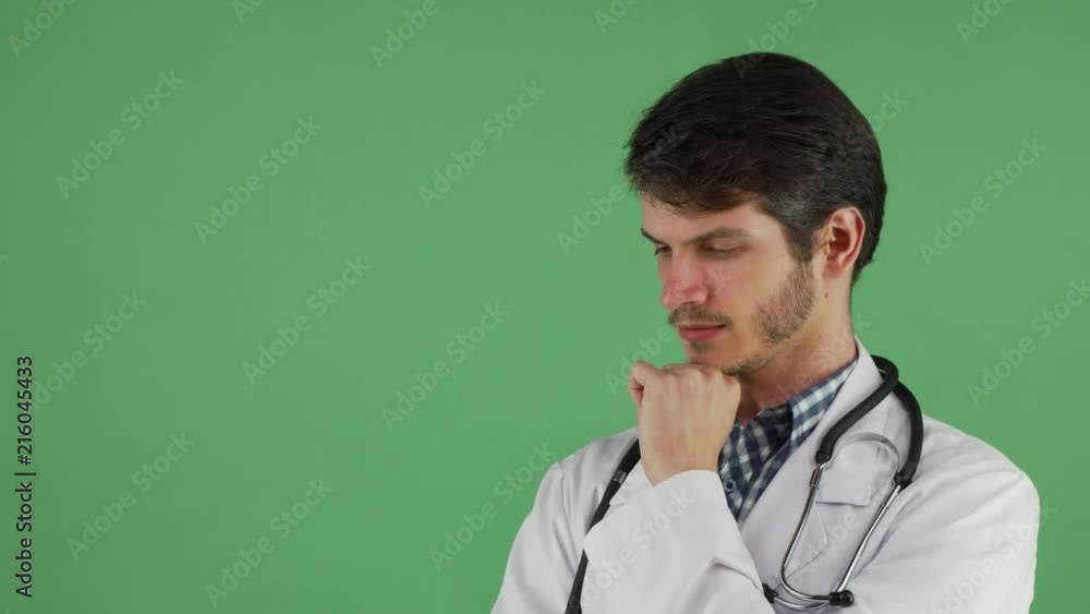 Portrait of a young handsome doctor posing on green chromakey background. Thoughtful male practitioner thinking rubbing his chin, copy space on the side. Experience, medicine concept. Portrait of a young handsome doctor posing on green chromakey background. Thoughtful male practitioner thinking rubbing his chin, copy space on the side. Experience, medicine concept.