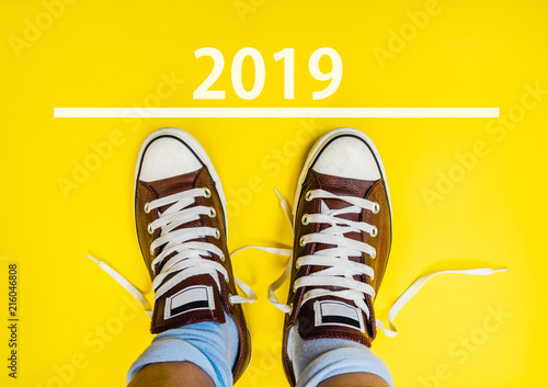 happy new year 2019. man legs in sneakers standing next to line and number 2019 on yellow background