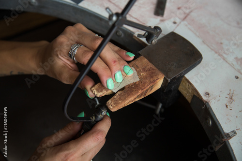 The process of making silver jewellery. Cutting a raw silver blank with a jacksaw. Female artist hands close up. Crafting a silver ring, see the entire series.