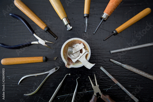 Top view jeweller's tools - pliers, cutters, carving knives, moulds, raw silver  pieces, engraver, sander, jeweler's bench pin