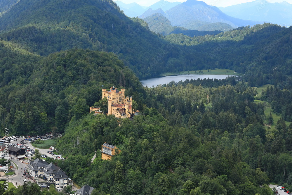 The picturesque foothills of the Alps, the lake surrounded with the low rocks overgrown with the dense wood are visible the old castle.