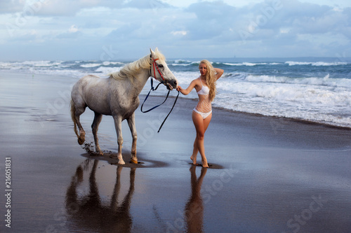 Beautiful young woman walking with horse at the beach, horseback photo