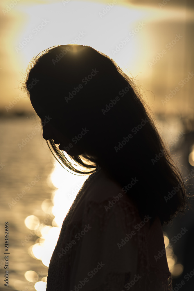 Silhouette of a young teenage girl against sunset at the beach, looking ...