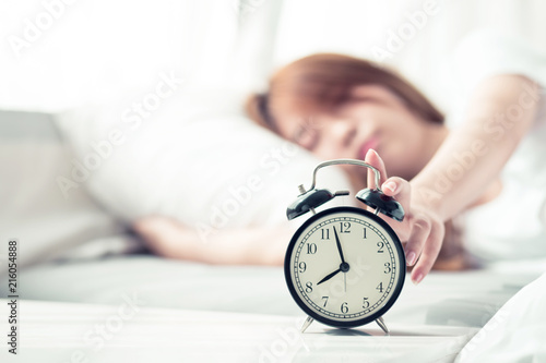 Beautiful asian young woman turn off alarm clock in morning, wake up for sleep with alarm clock, relax and lifestyle concept.
