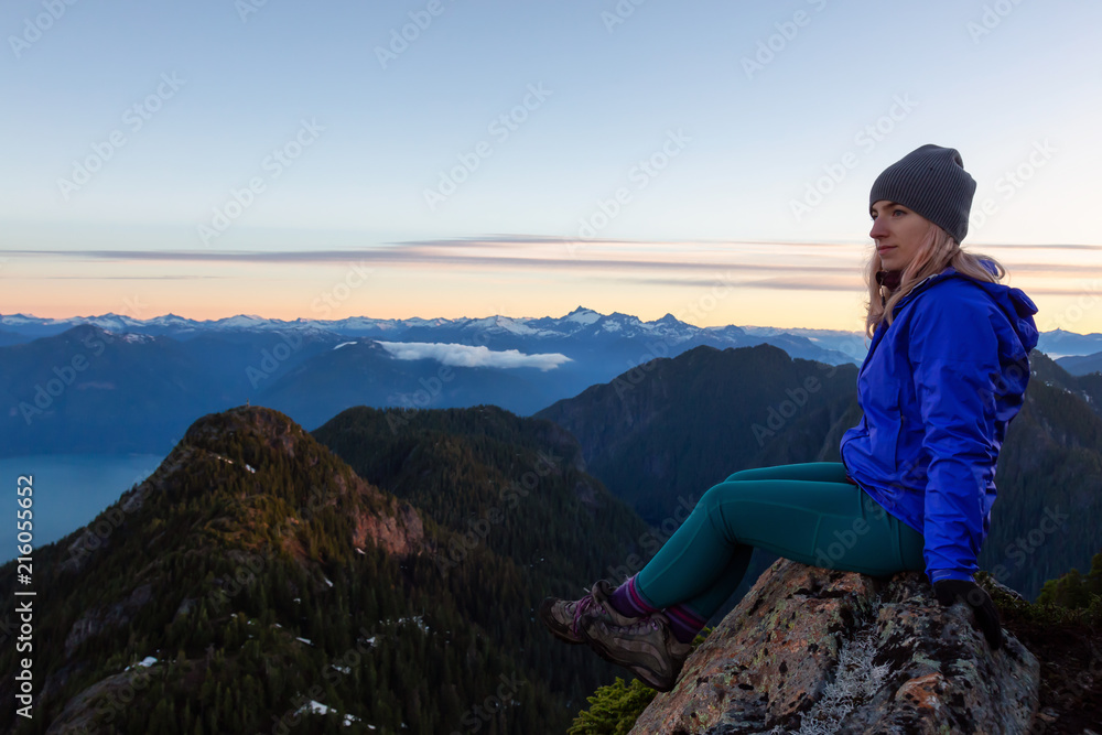 Adventurous woman on top of a mountain cliff is enjoying the beautiful summer sunrise. Taken on Mount Brunswick, Lions Bay, North of Vancouver, BC, Canada. Adventurous woman on top of a mountain cliff is enjoying the beautiful summer sunrise. Taken on Mount Brunswick, Lions Bay, North of Vancouver, BC, Canada.