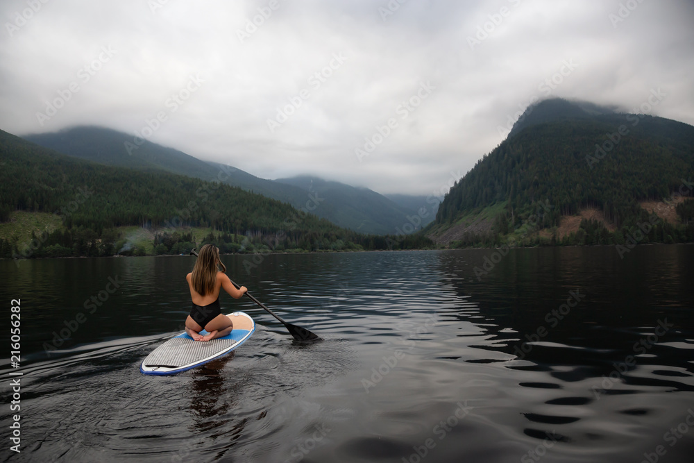 Young woman on a paddle board during a cloudy evening. Taken in Jones Lake, near Hope and Chilliwack, East of Vancouver, BC, Canada.