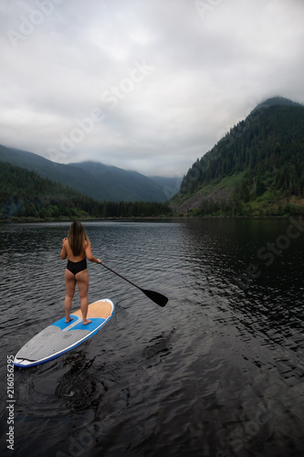 Young woman on a paddle board during a cloudy evening. Taken in Jones Lake, near Hope and Chilliwack, East of Vancouver, BC, Canada.