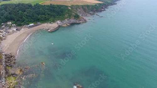 4K Cornwall Aerial over Par Sands beach and surrounding coast and Polkerris harbour and beach. Flying over fields with sheep and cows with lush green grass along the South west coast path. photo