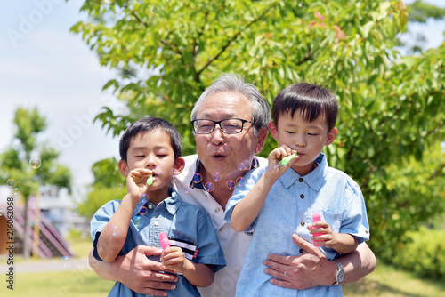 公園でシャボン玉を楽しむ孫を抱きしめるシニア男性