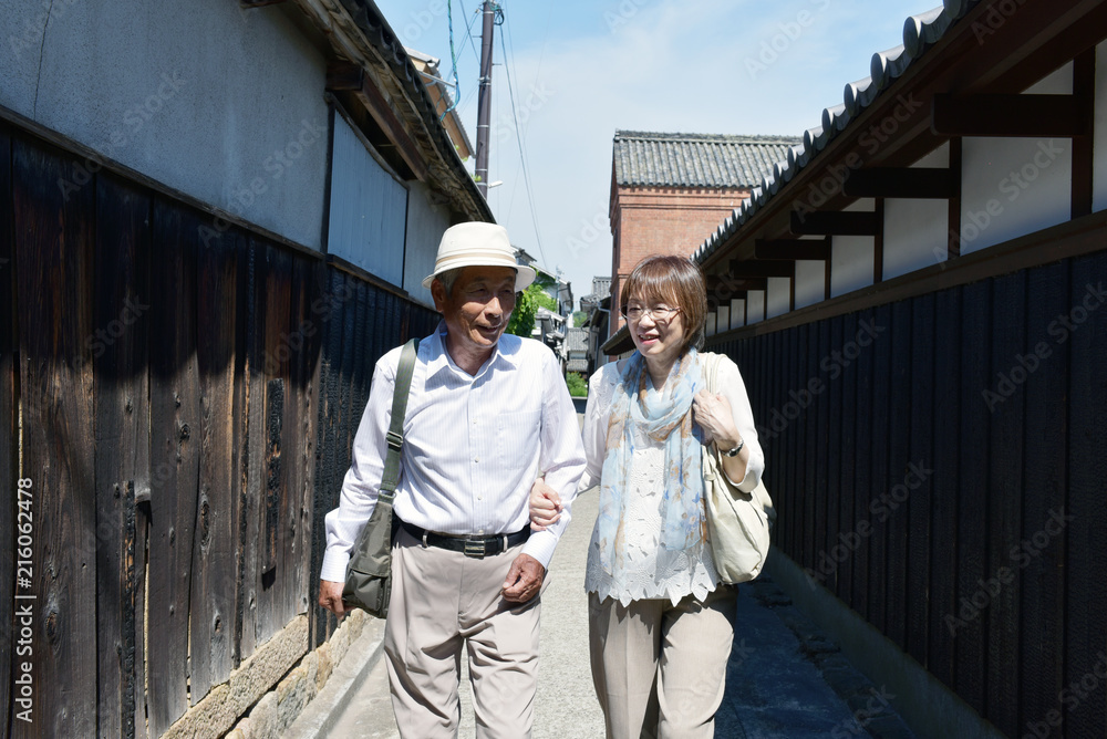 腕を組み歩く観光地の路地を歩くシニア夫婦 腕を組み歩く観光地の路地を歩くシニア夫婦