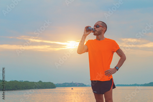Tired jogger making a pause and drinking water.