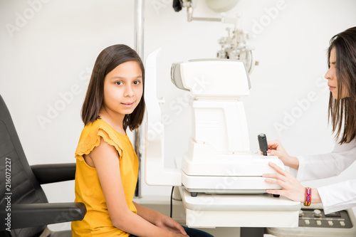 Attractive little girl sitting on chair for eye test while looking at camera