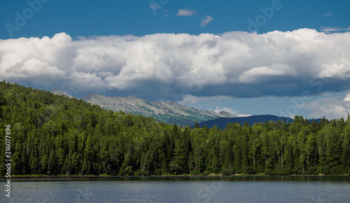 panorama of the forest on the lake behind which you can see the mountains over which stretched long white clouds