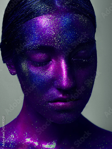Glowing neon makeup with dramatic look in his eyes. Creative body art on the theme of space and stars. Amazing close-up portrait glow in the bright dark makeup