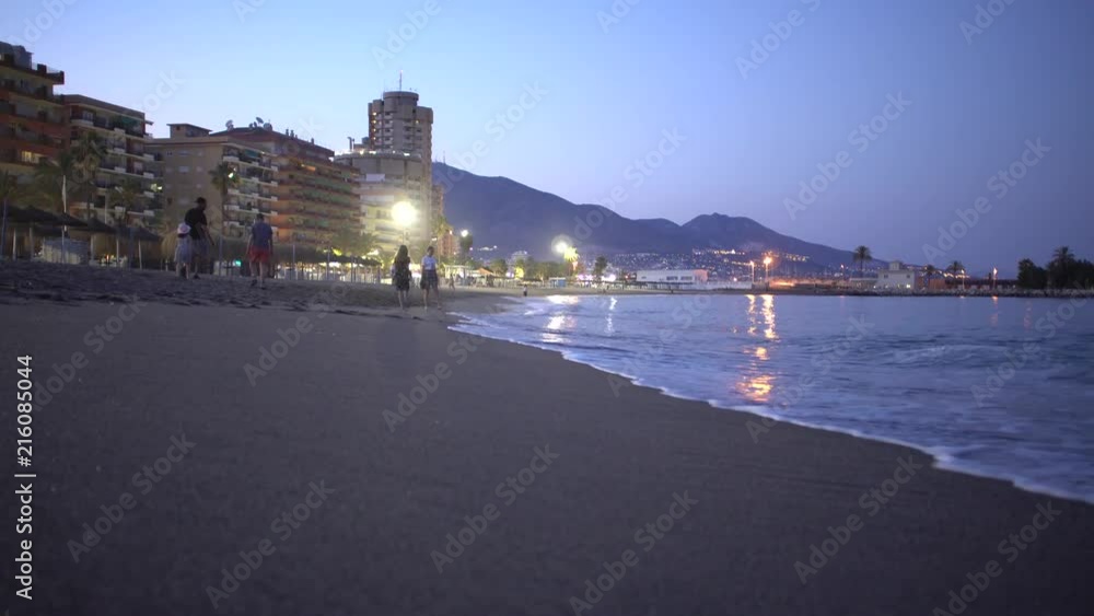 Beach view with sea waves close up with people walking forward in mediterranean spanish city - evening Beach view with sea waves close up with people walking forward in mediterranean spanish city - evening