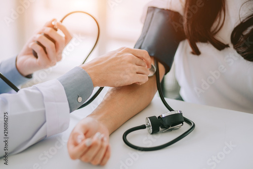 Doctor using sphygmomanometer with stethoscope checking blood pressure to a patient in the hospital.