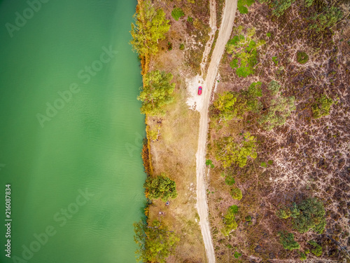 Looking down at small red car parked on the shore of Murray River in South Australia - aerial view