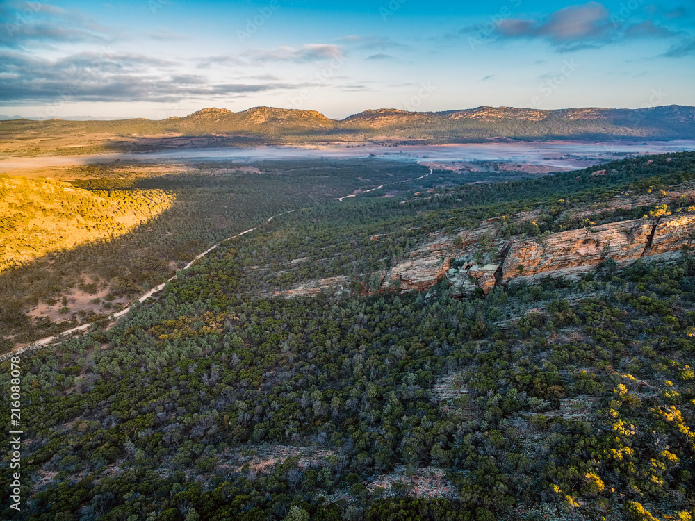 Fototapeta premium Dirt road winding through hills and native vegetation at sunrise - Flinders Ranges, South Australia
