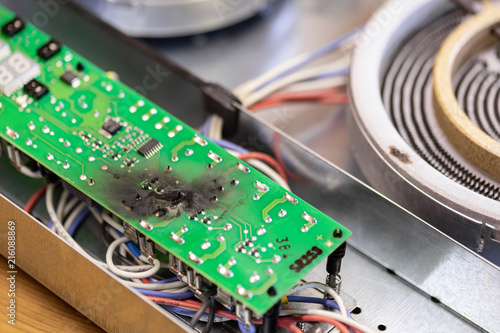 Burnt green microchip after short circuit due to water damage. Damaged overheat control panel board of cooking stove photo