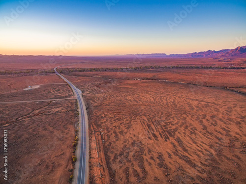Aerial view of road passing through red desert land at sunset