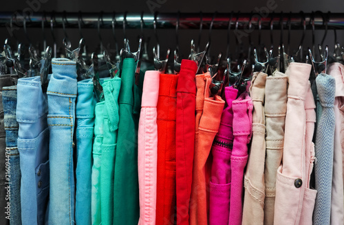Many colorful fabric jeans are hanging on the clothesline, as abstract color fashion background.