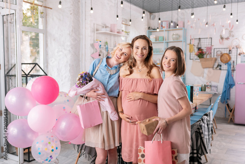 Sisters and presents. Two beautiful women standing near their pregnant sister with presents while visiting event agency