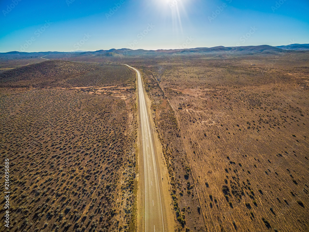 Rural road passing through dry land with scarce vegetation on bright sunny day - aerial view