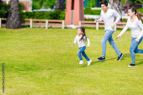 Little girl is running with parents in the park. Young family with little kid having fun in nature.