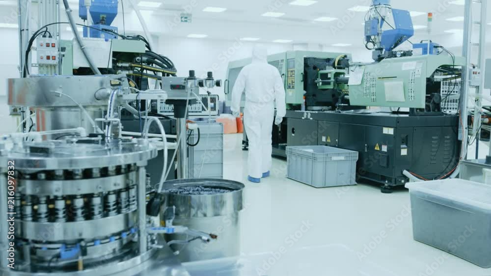 On a Factory Scientist in Sterile Protective Clothing Work on a Modern Industrial 3D Printing Machinery. On a Factory Scientist in Sterile Protective Clothing Work on a Modern Industrial 3D Printing Machinery.