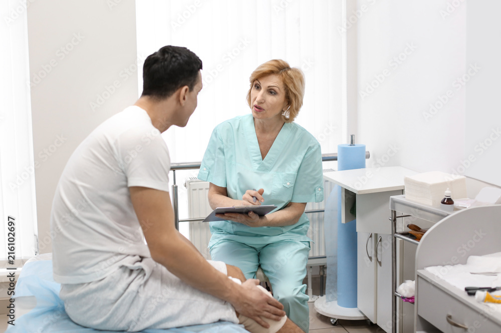 Fototapeta premium Orthopedist and patient with bandaged leg in hospital