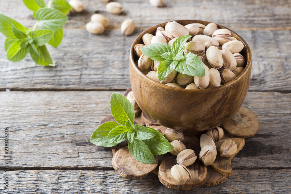 Delicious salted pistachios and fresh mint leaves on wooden background. Delicious salted pistachios and fresh mint leaves on wooden background.