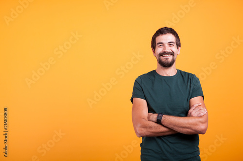 Handsome man with his arms crossed smiling at the camera isolated on yellow background. Portrait of attractive bearded confident person in studio photo