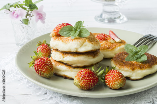 Curd pancakes with strawberries and mint on a plate.