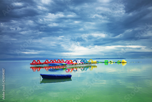 Lake Balaton before storm in Hungary. Tranquil scene with nice cloudscape, colorful pedalos and a blue boat in the front photo