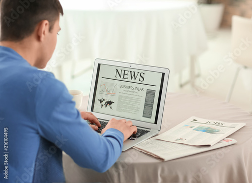 Young businessman reading news on laptop screen in cafe