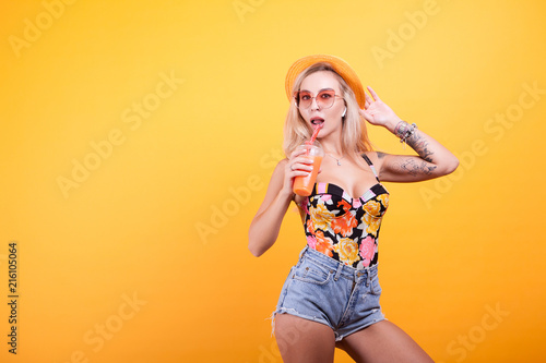 Attractive young woman drinking orange juice with sunglasses in studio