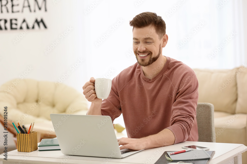 Freelancer drinking coffee while using laptop at home