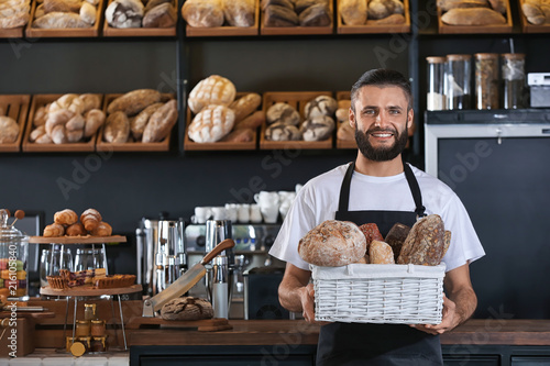 Fotografiet Male baker holding wicker basket with fresh bread in shop
