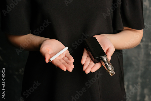 Close-up view of female hands holding an e-cigarette in one hand and nicotine cigarette in another one. Choice concept.Differences in taste and preference
