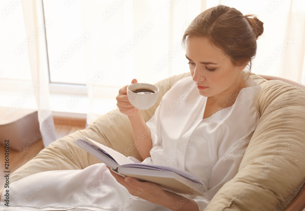 Young woman drinking coffee while reading book on lounge chair at home Young woman drinking coffee while reading book on lounge chair at home