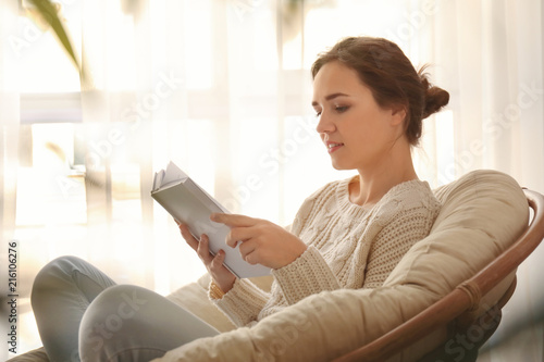 Young woman reading book on lounge chair at home